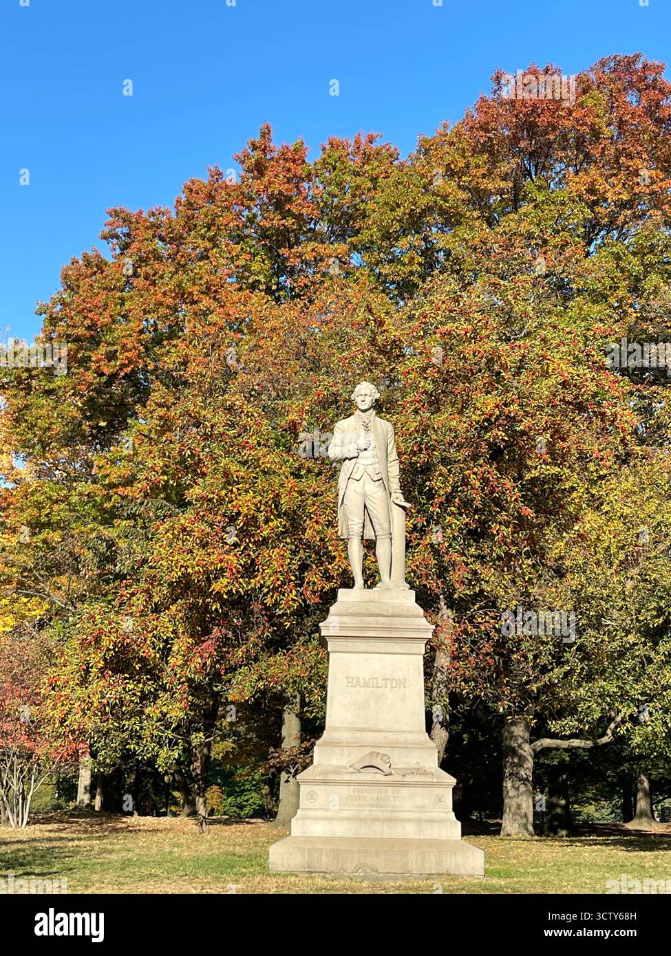 The statue of Alexander Hamilton in Central Park, New York City, surrounded by the vibrant colors of fall foliage. - Smartphone Captured Stock Image