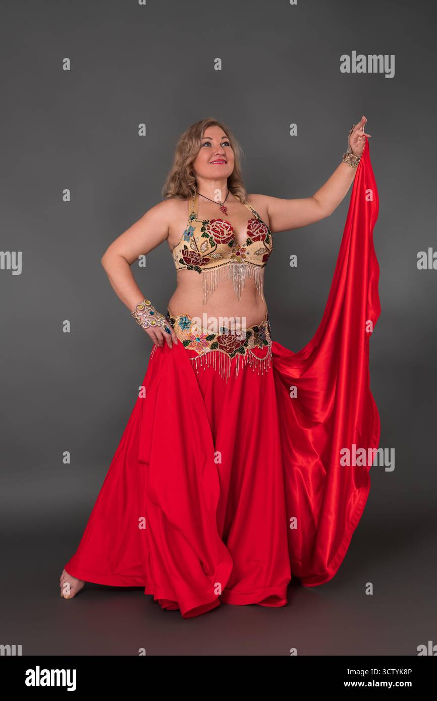 Smiling and happy curvy woman dancer dressing in dancing costume - bra top and red maxi skirt, she is not wearing any footwear, performing in full len Stock Photo