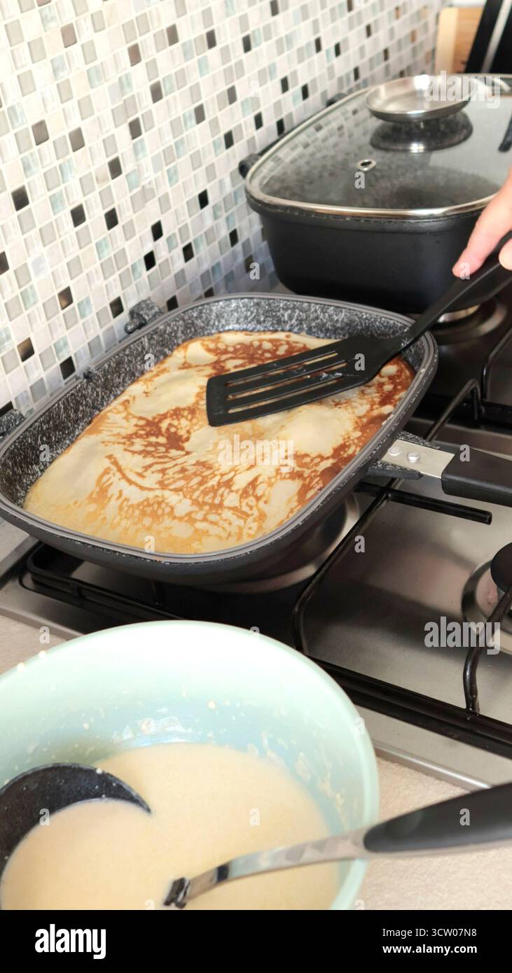 Anonymous person fries pancake in rectangular nonstick pan. This homemade pancake is made in kitchen using organic, gluten-free ingredients. Stock Photo