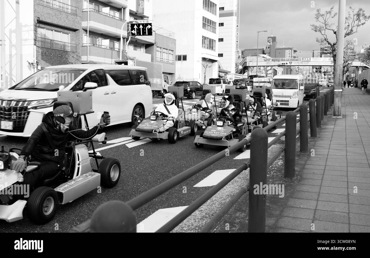 Tourists dressed in costumes drive go-karts through the streets of Osaka in black & white Stock Photo