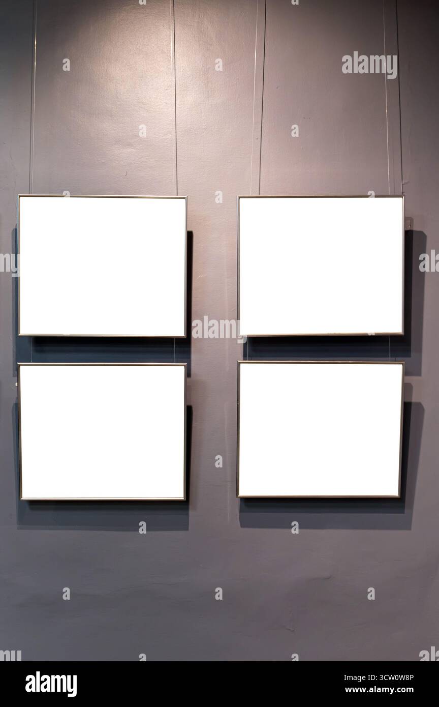 Four rectangular frames with white blank space hang on a grey wall by thin wires. Stock Photo