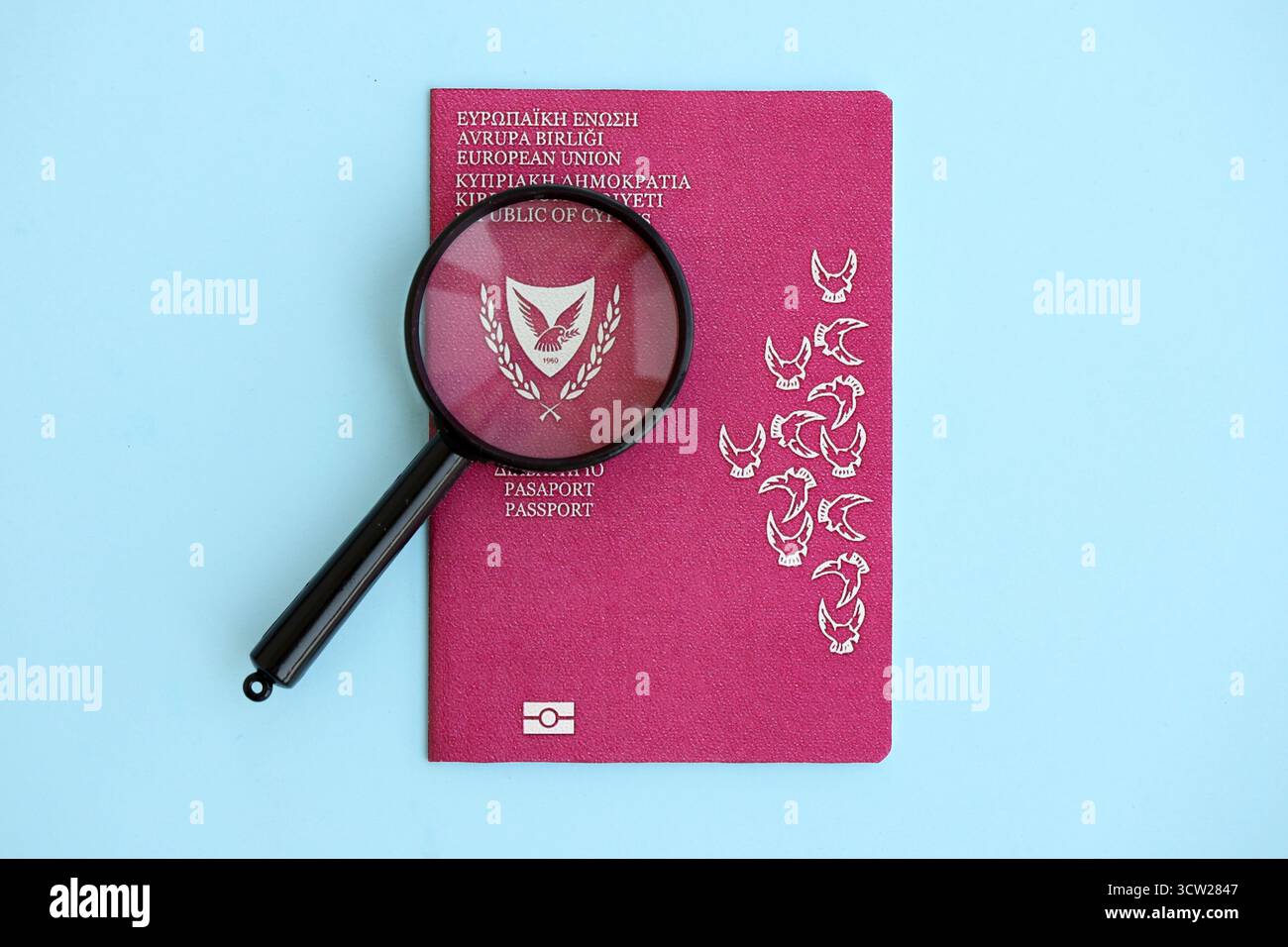 Kyprus passport and magnifying glass on light blue paper background close up. Citizenship details and information concept Stock Photo