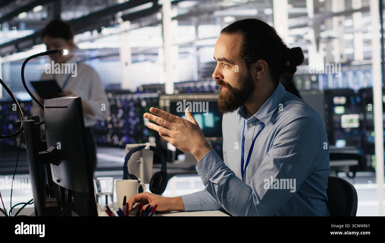 Data center technician discussing with coworker while doing AI software updates. Server room IT specialist and colleague chatting, optimizing infrastructure using artificial intelligence, camera A Stock Photo