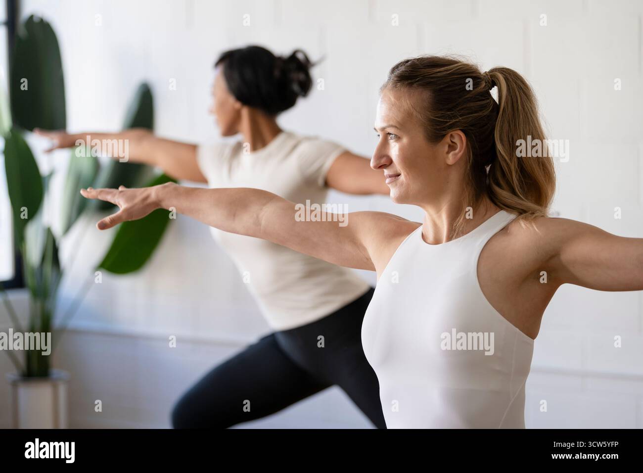Two women practicing yoga poses during class Stock Photo