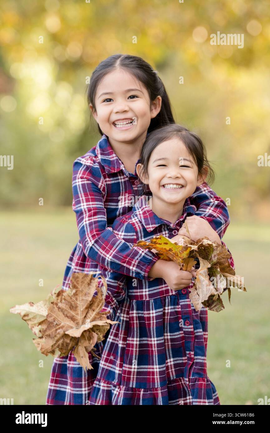 Sisters hugging in autumn with big smiles and leaves Stock Photo - Alamy
