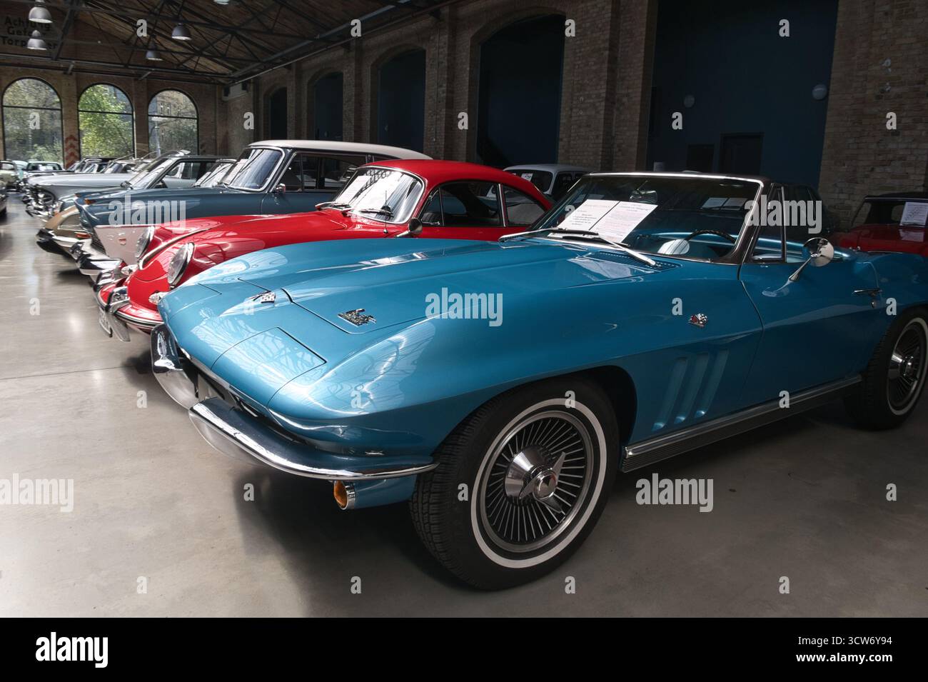 Iconic Blue Corvette Sting Ray Roadster - A classic blue American convertible with whitewall tires sits in a row of vintage cars inside a spacious, li Stock Photo