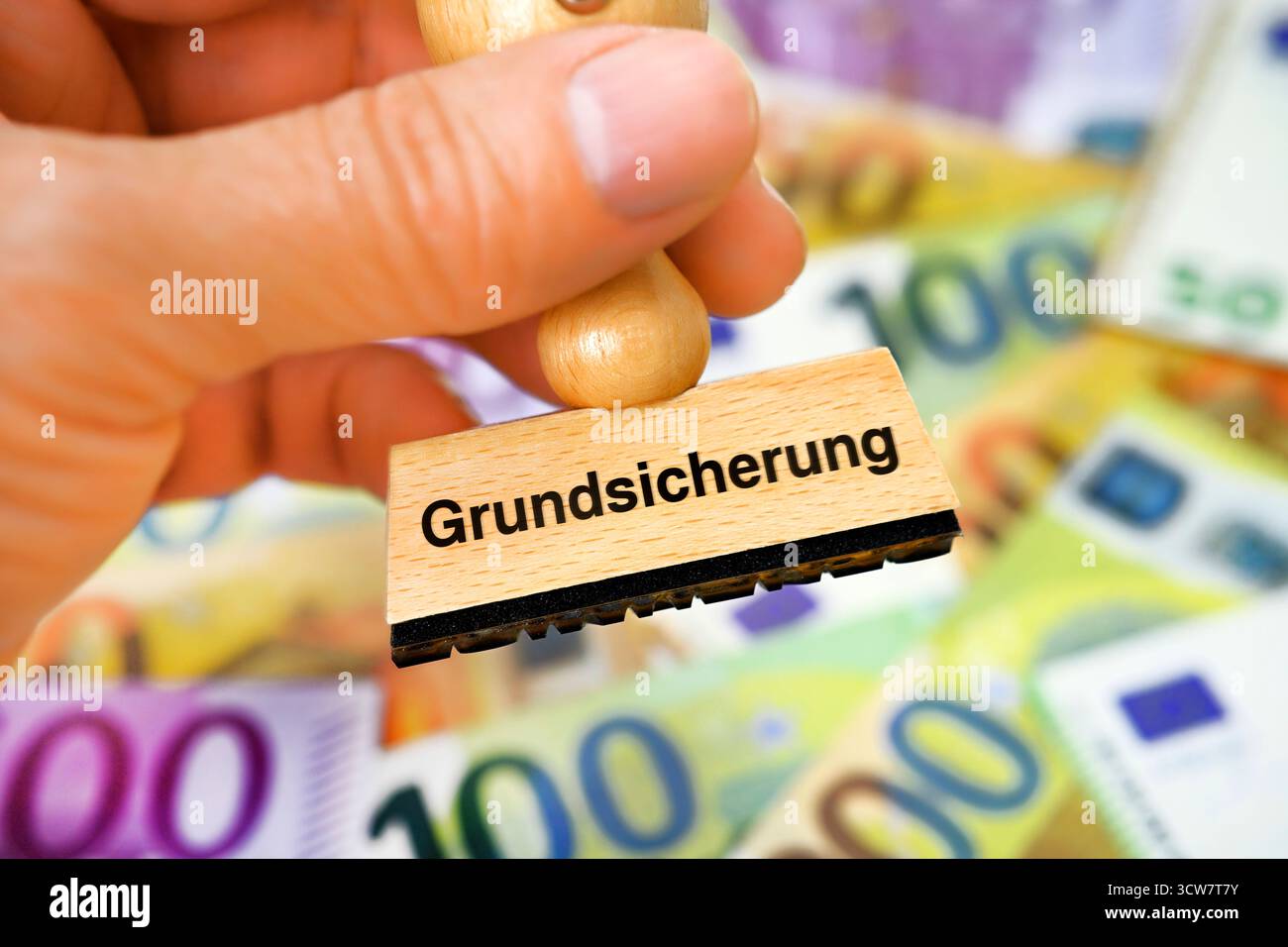 Stamp Geld FOTOMONTAGE, Hand hält Stempel mit Aufschrift Grundsicherung vor ...