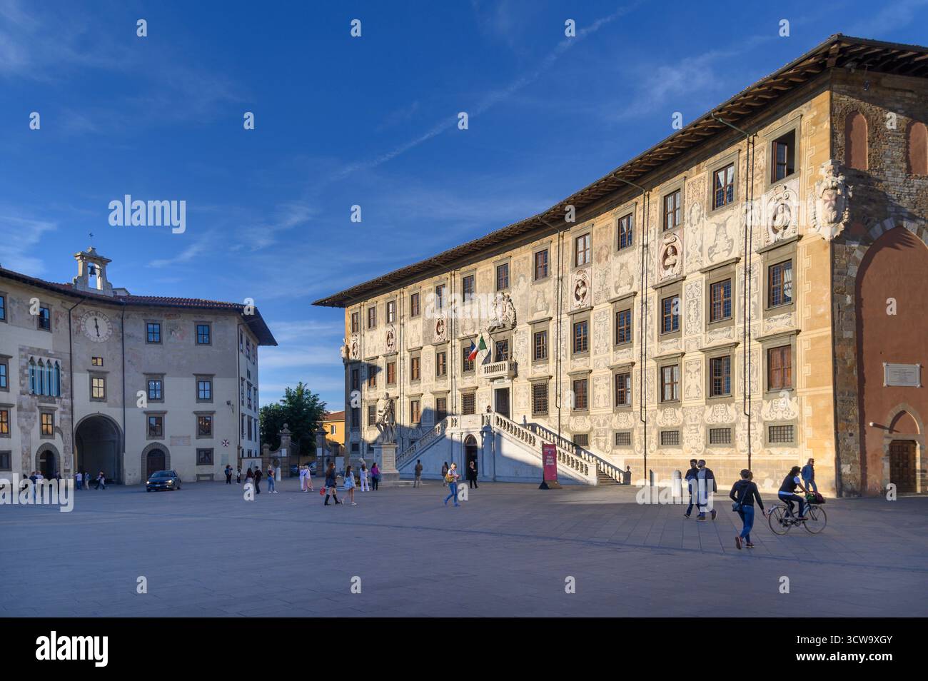 Piazza dei Cavalieri, Pisa. Historic square framed by the Palazzo della Carovana and Palazzo dell'Orologio under a clear blue sky, bustling with life Stock Photo