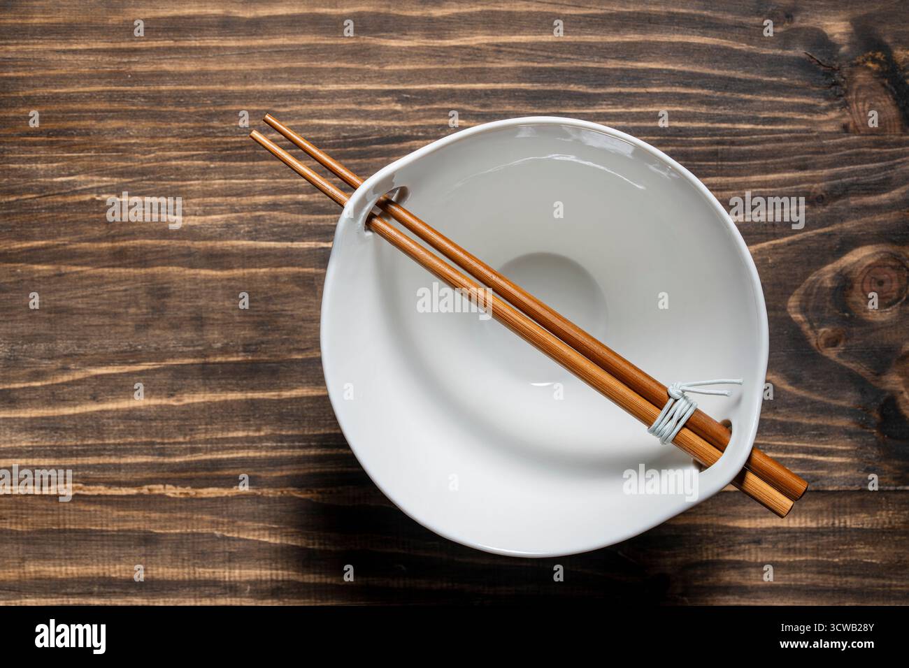 A pair of chopsticks lying across an empty white soup bowl on wooden table, close up, top view Stock Photo