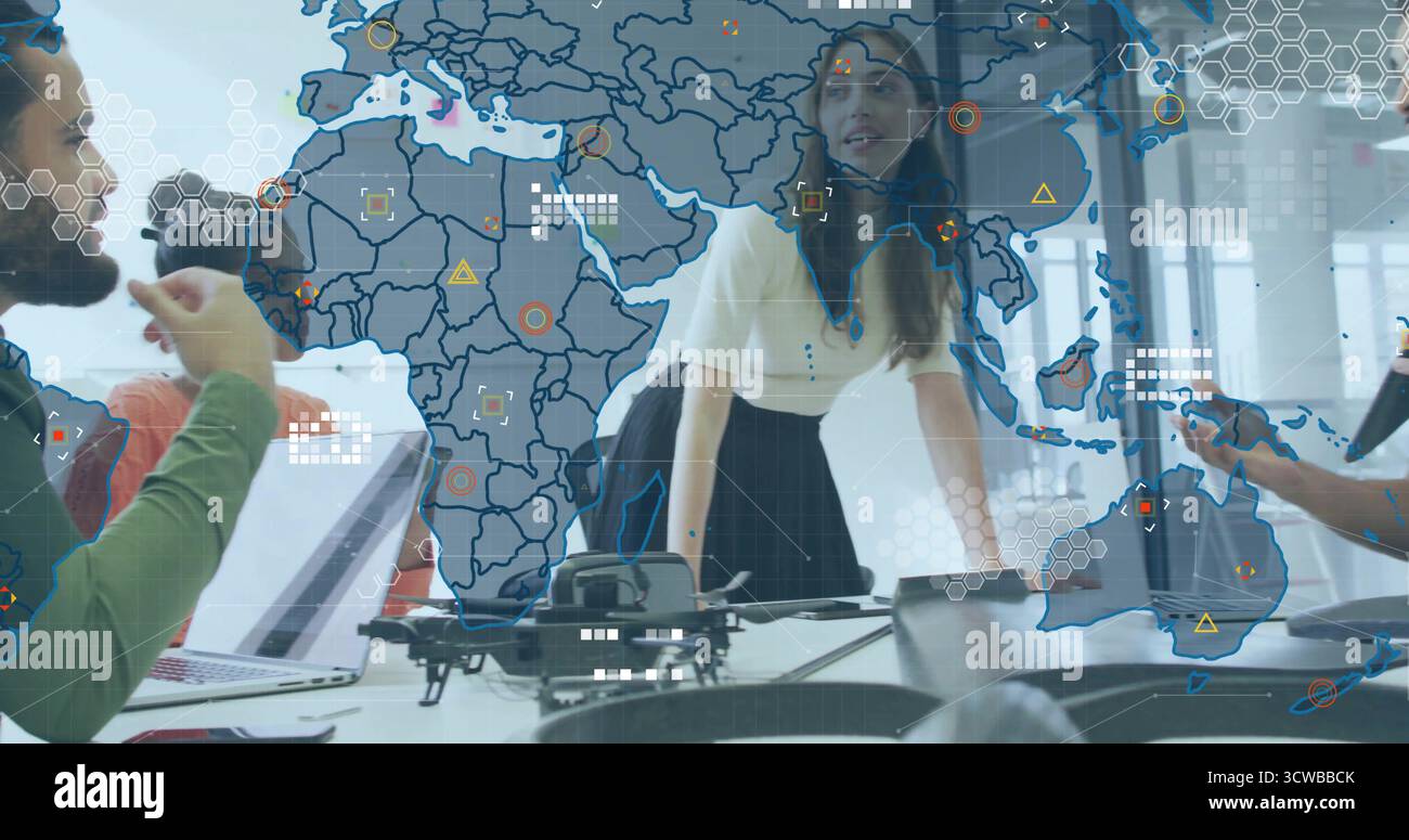 Collaborating colleagues examining drone and discussing data on digital map and laptops in office Stock Photo