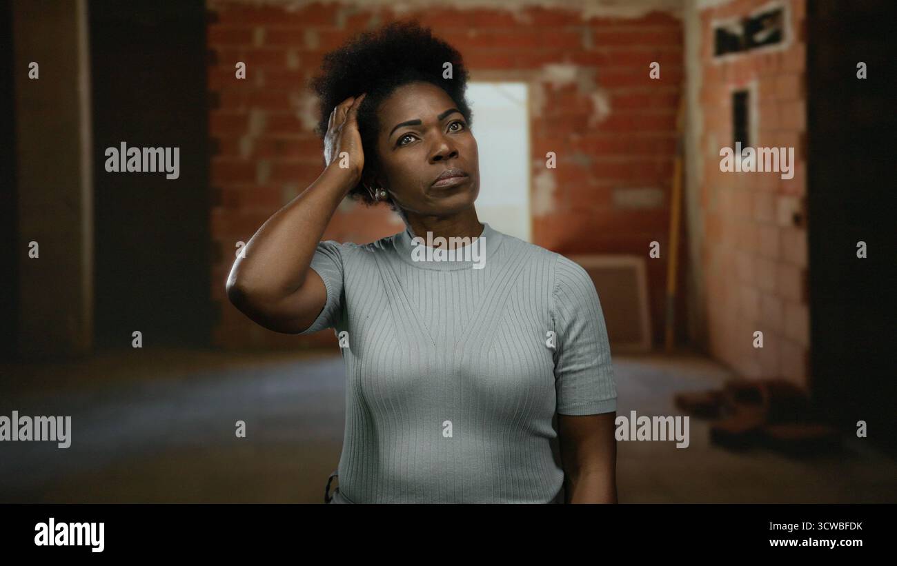 Woman contemplating in an incomplete indoor construction site wearing casual attire with a focused expression suggesting deep thought in an urban sett Stock Photo
