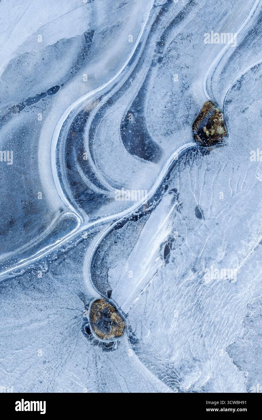 Two small stones locked in a sheet of swirling frozen ice, creating an abstract pattern of curves and arcs - Stock Image