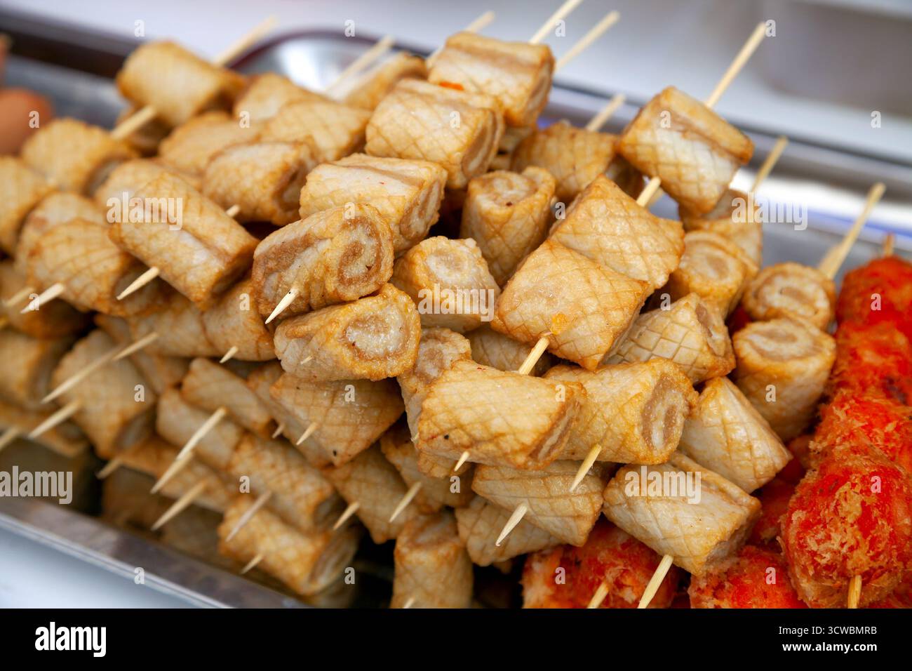 A large pile of Vietnamese skewered snacks sits ready to eat at an outdoor market stall. Tasty cooked rolls are stacked high for sale at a market - Stock Image
