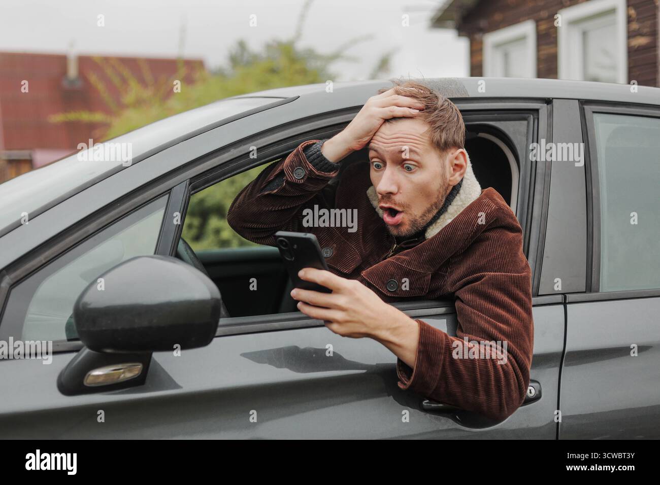 Shocked man sitting inside car with smartphone in hand. Stock Photo