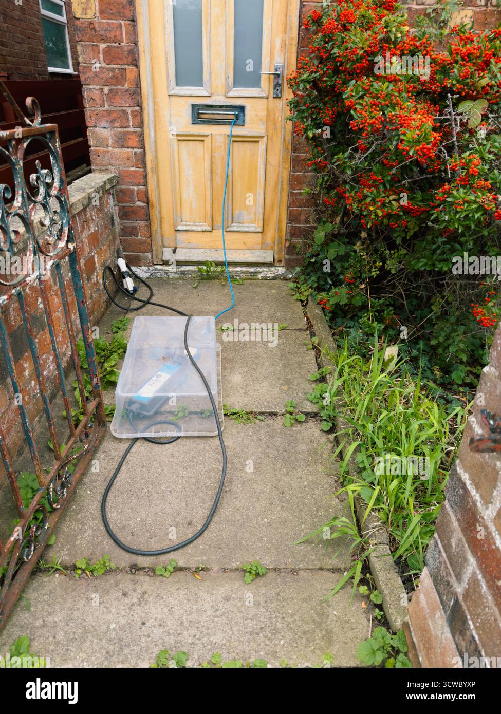 What is often reffered to as a granny charger on a front path with the cable passing through the letterbox of the front door of a cottage. - Smartphone Captured Stock Image