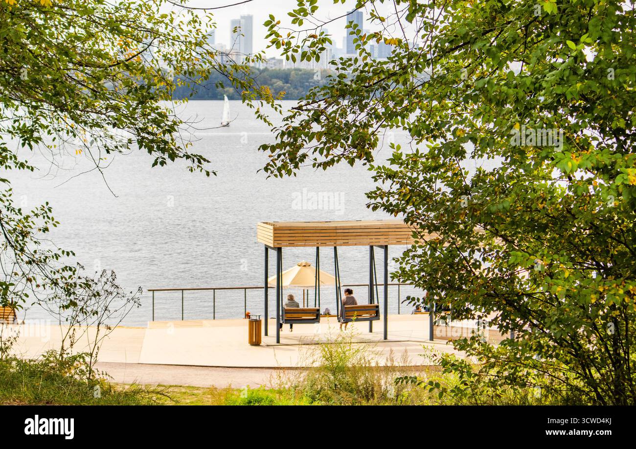 Urban waterfront by the lake with gazebo and benches, framed by foliage ...