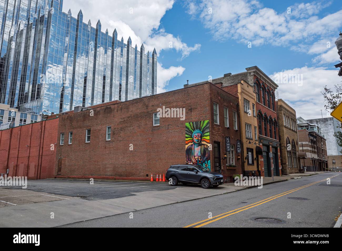 A striking Buddha mural on a historic brick building contrasts with the towering, modern glass architecture of PPG Place in Pittsburgh. Stock Photo