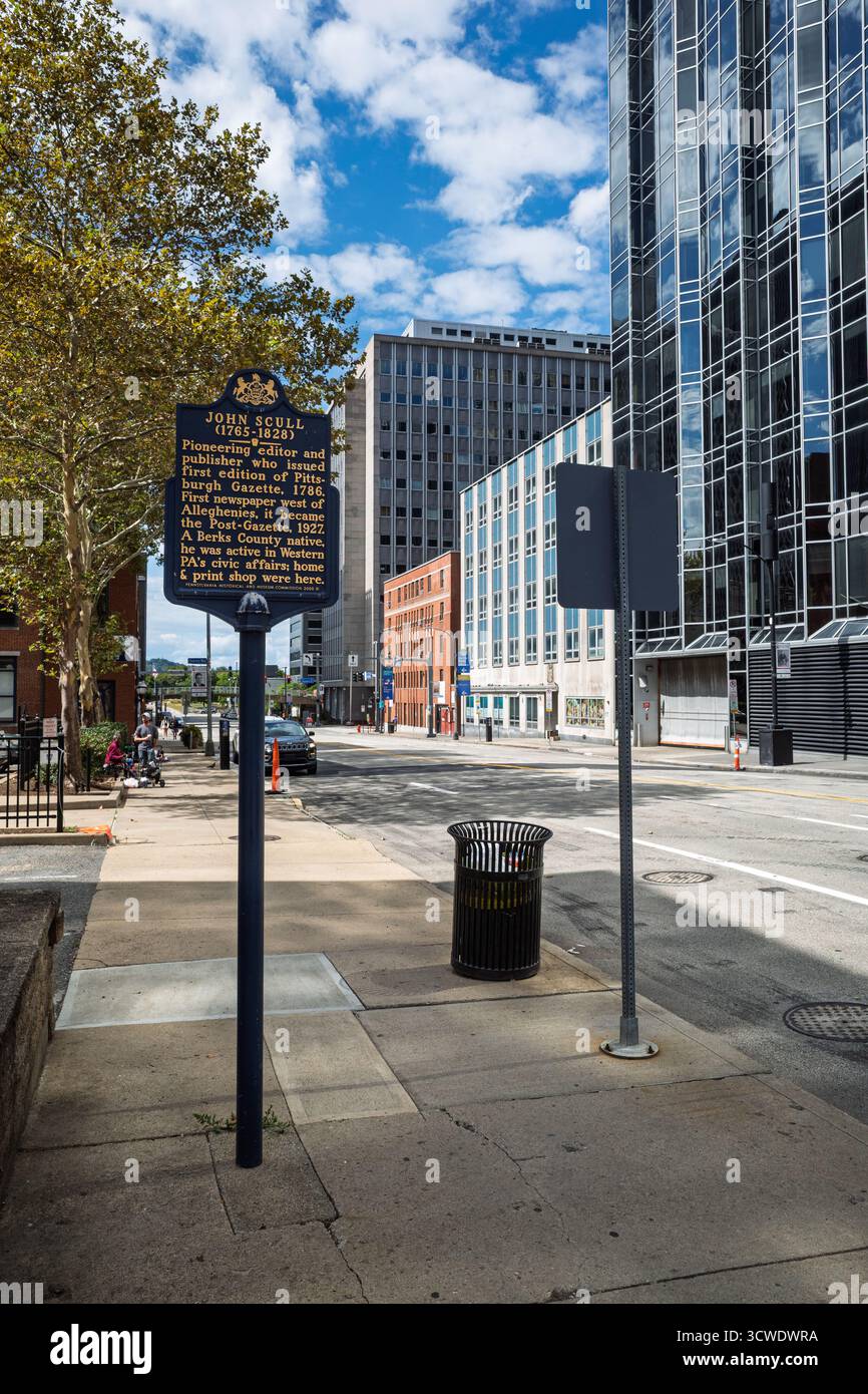 A historic marker for John Scull, founder of the Pittsburgh Post-Gazette, on a sidewalk lined with modern and traditional downtown buildings. Stock Photo