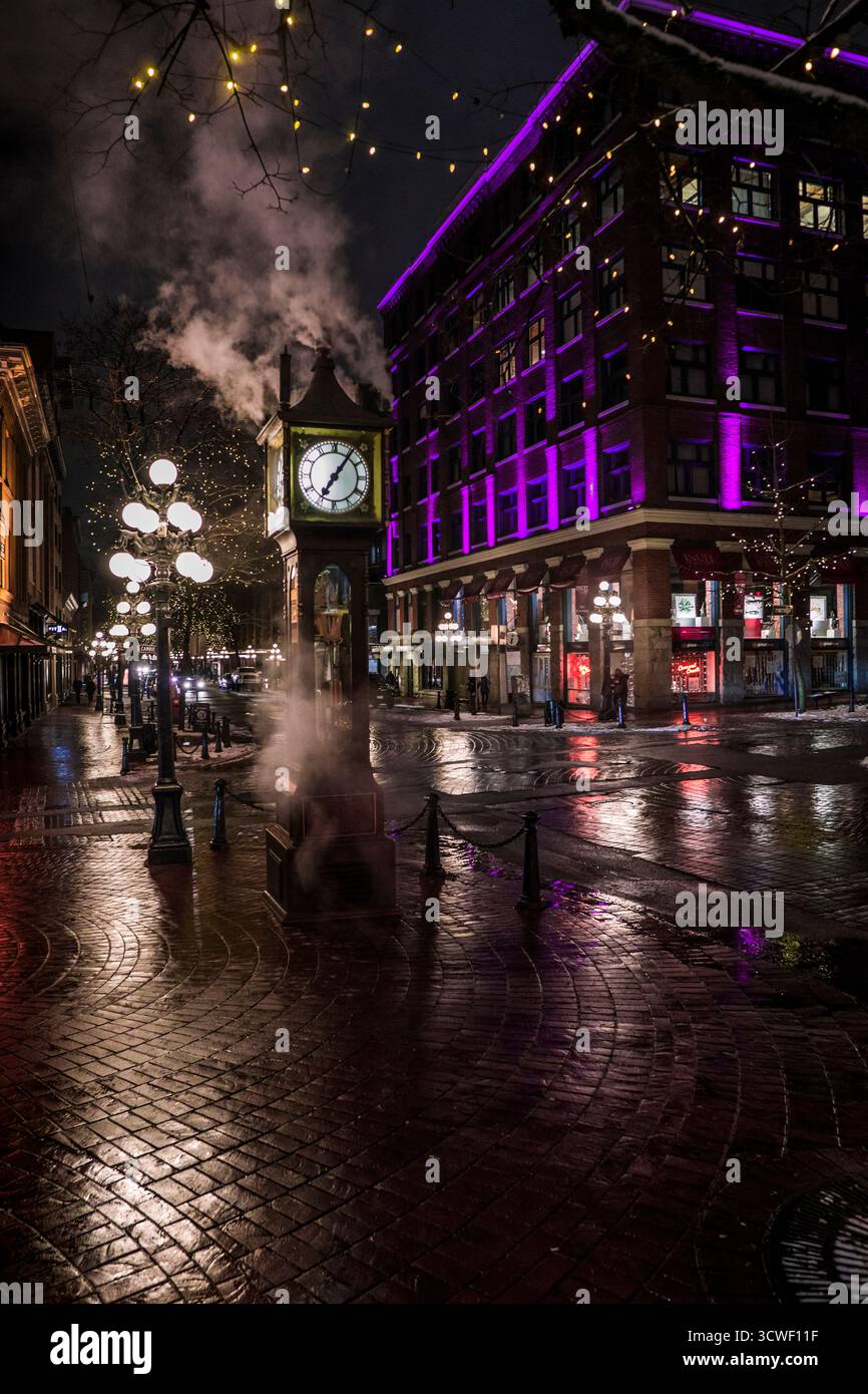 A steam-emitting clock tower stands in a bustling downtown area at ...