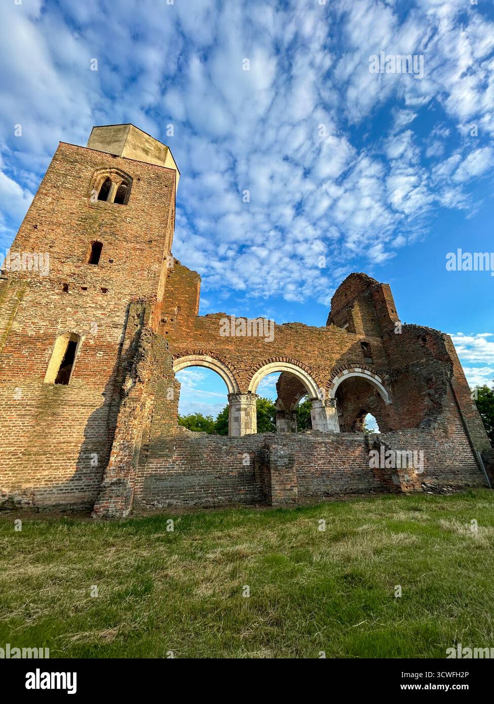 Historic brick church ruins with arched windows and tower under a bright blue sky with scattered clouds, symbolizing heritage and time. - Smartphone Captured Stock Image