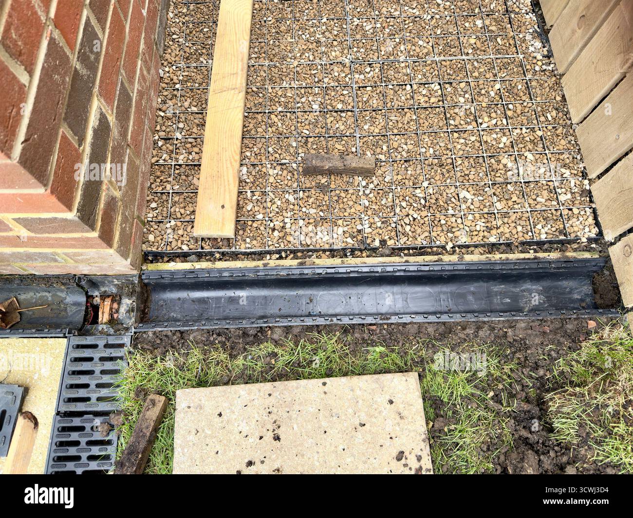 Close-up of construction site showing brick wall, metal grid, gravel, and wooden planks on a foundation preparation area - Smartphone Captured Stock Image