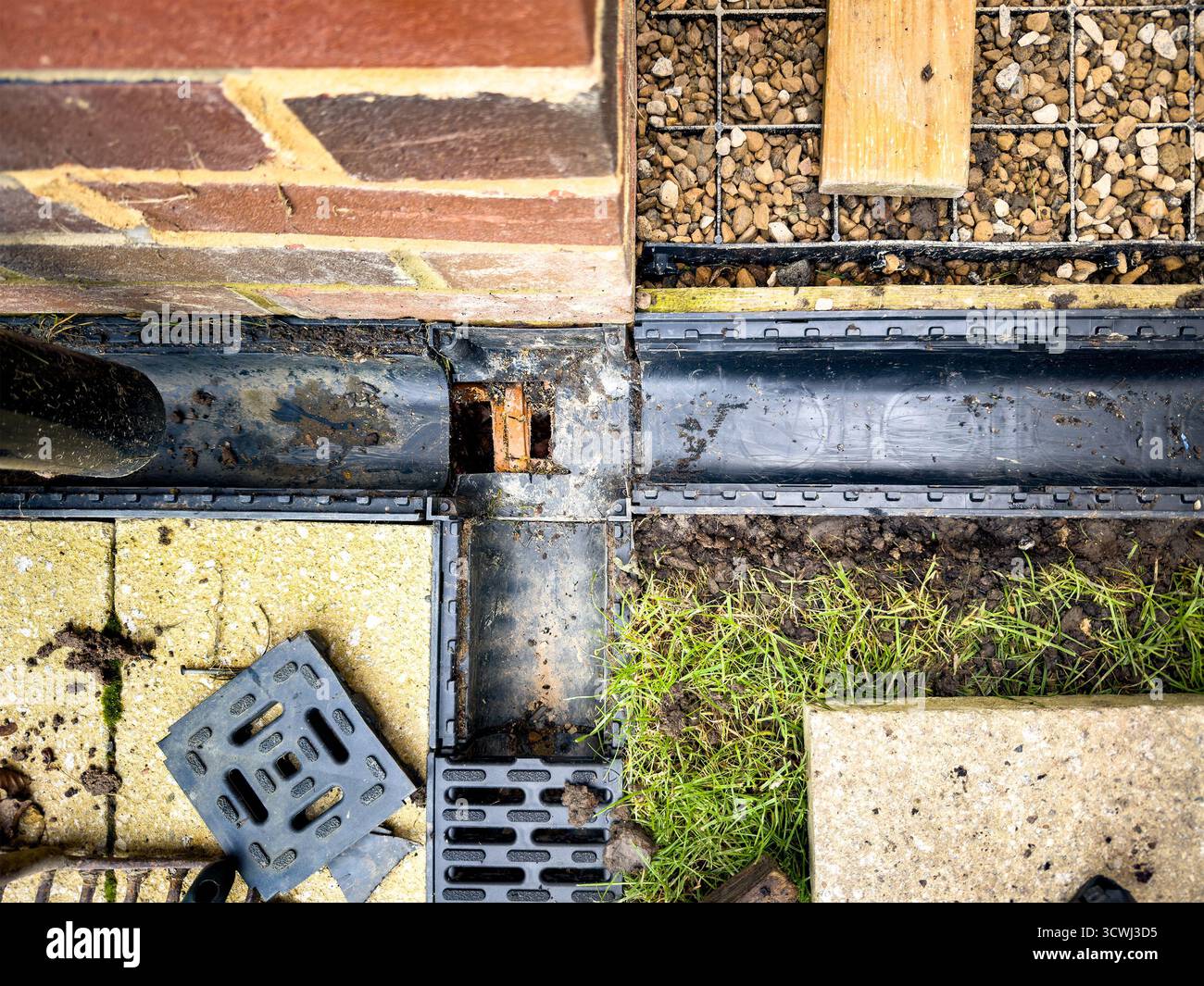 Overhead view of drainage system installation with brick wall, plastic components, and grass in the background - Smartphone Captured Stock Image