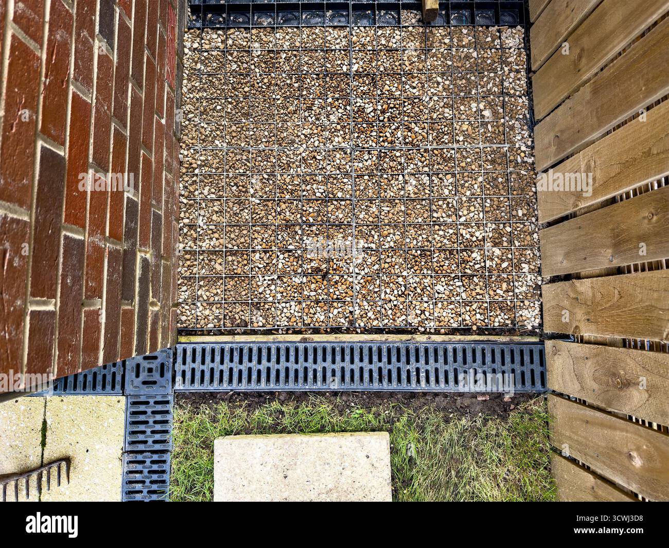 Overhead view of a small gravel area enclosed by red brick and wooden fences with drainage grates visible - Smartphone Captured Stock Image