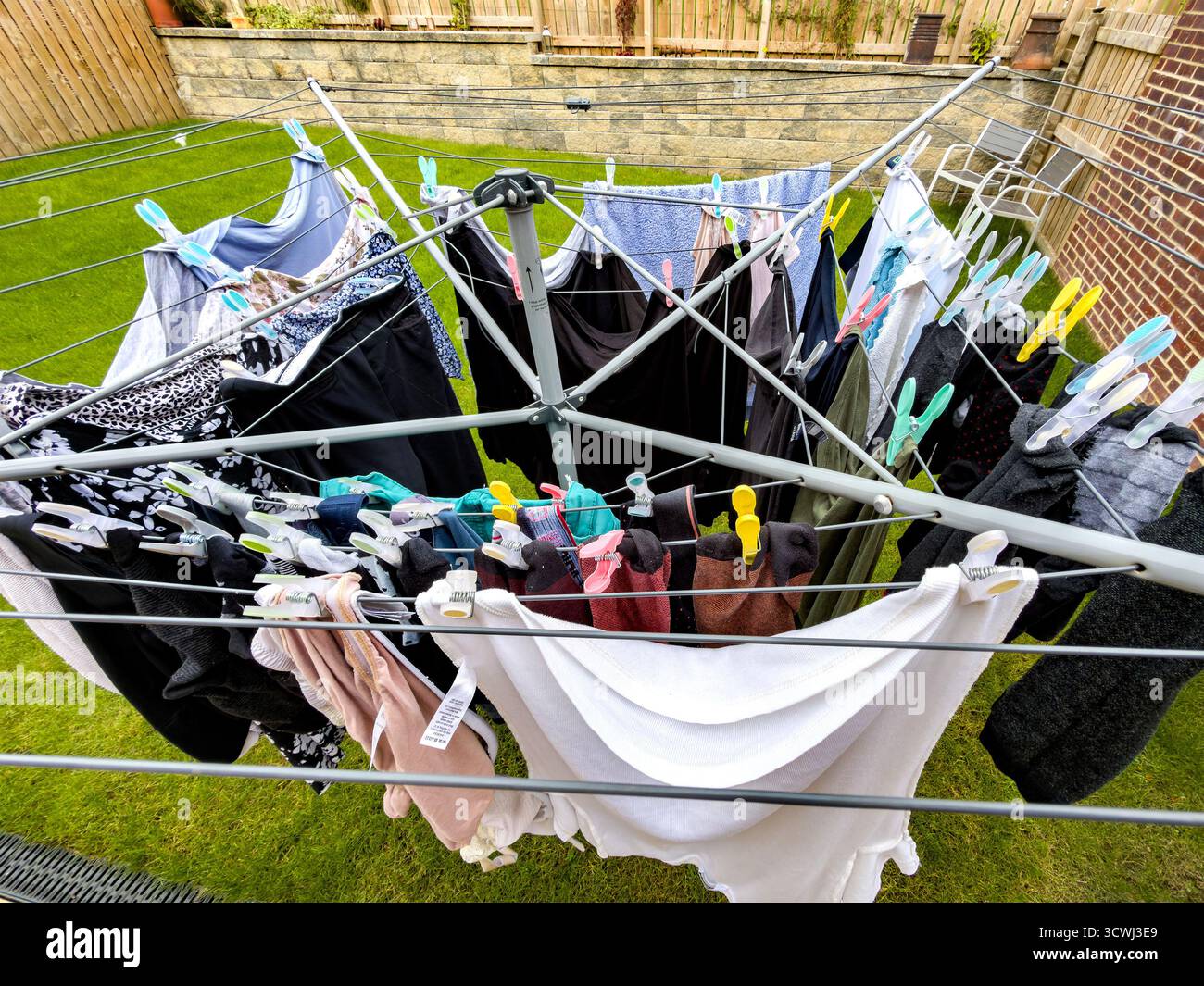 high view Colourful clothes hanging on a rotary dryer in a backyard garden on a sunny day surrounded by a stone wall and wooden fence uk - Smartphone Captured Stock Image