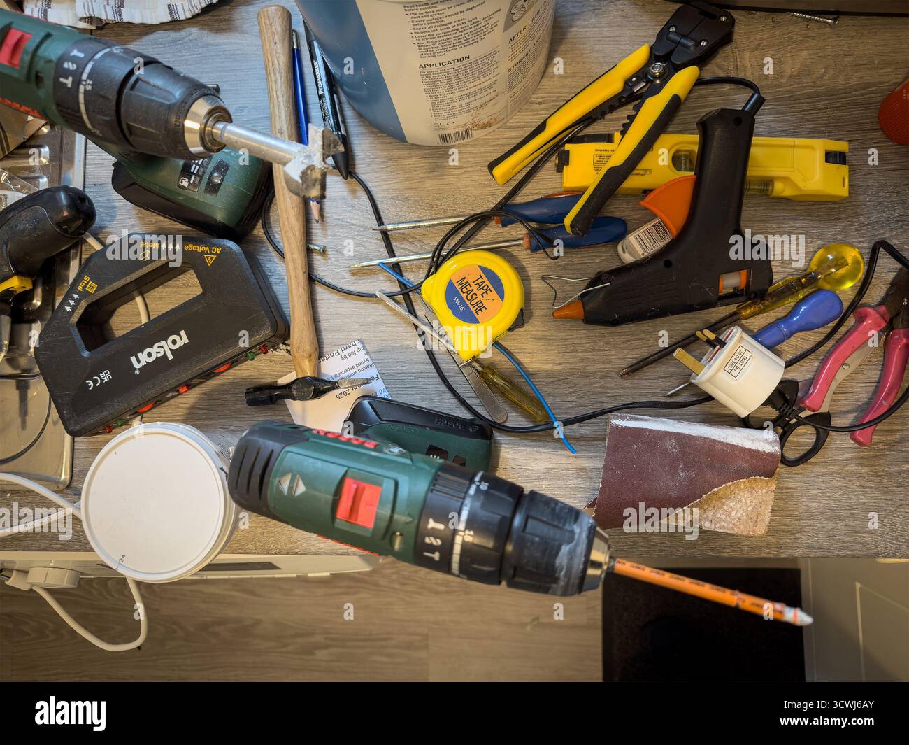 A cluttered workbench with various tools including drills, measuring tape, wire strippers, and hand tools for home improvement projects - Smartphone Captured Stock Image