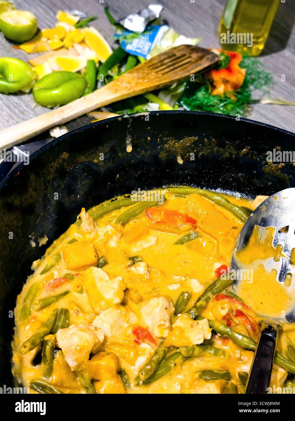 Thai chicken curry Laksa cooking in a black wok pot with fresh ingredients and a messy kitchen background - Smartphone Captured Stock Image