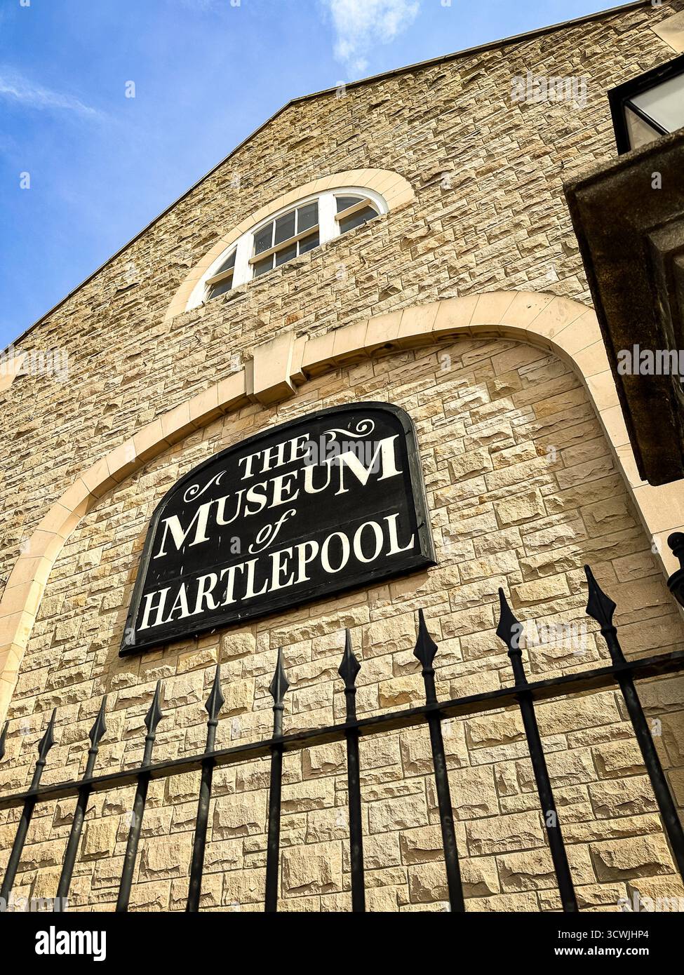 View of the Museum of Hartlepool with arched windows, brick facade, and a wrought iron fence under a clear, blue sky - Smartphone Captured Stock Image