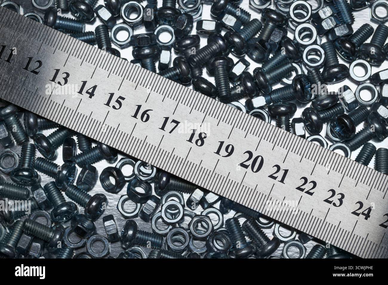 Lots of small screws and nuts scattered in a heap and a metal ruler Stock Photo