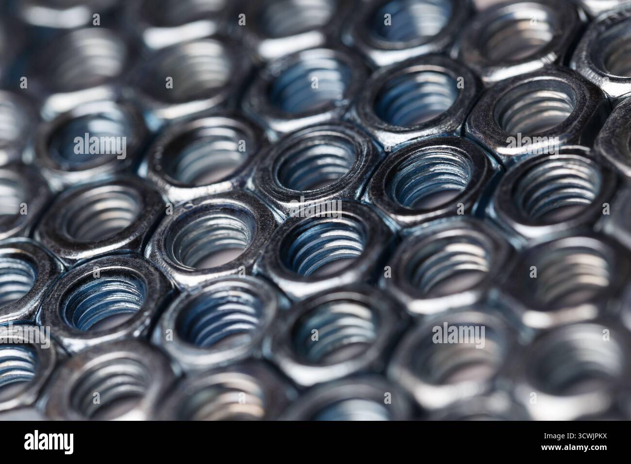 Shiny metal nuts arranged in a precise order. Diagonal composition with selective focus. Stock Photo