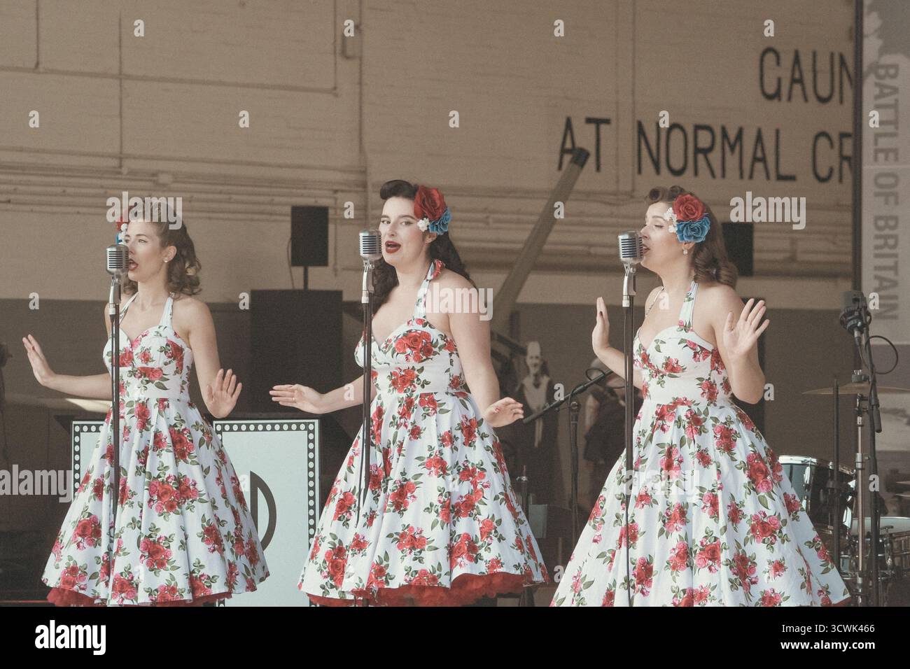 Three female singers in vintage floral dresses performing at outdoor event Stock Photo