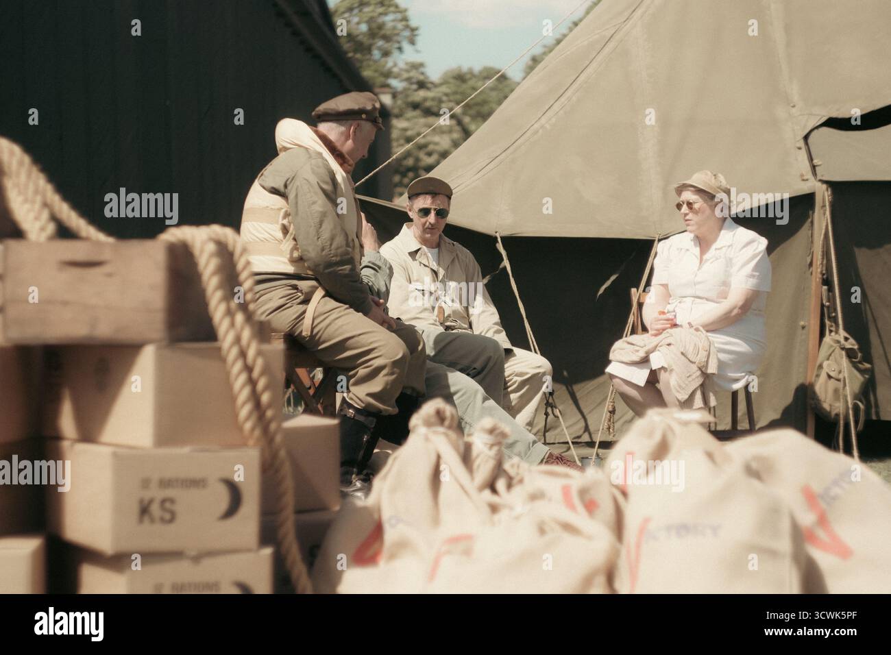 Three WWII servicemen relaxing at military camp with tents and supplies Stock Photo