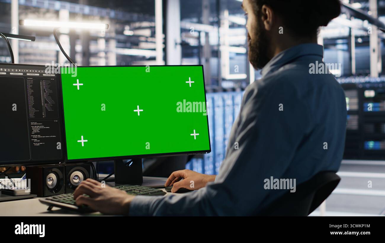 Data center technician doing software updates using green screen mockup computer. Server room IT specialist , optimizing infrastructure using chroma key isolated screen PC, camera A Stock Photo
