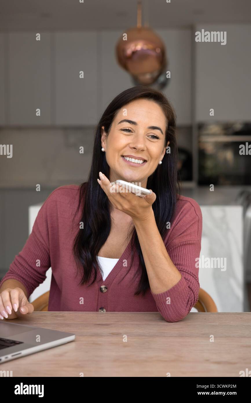 Positive Hispanic freelance worker woman talking on speaker on cellphone Stock Photo
