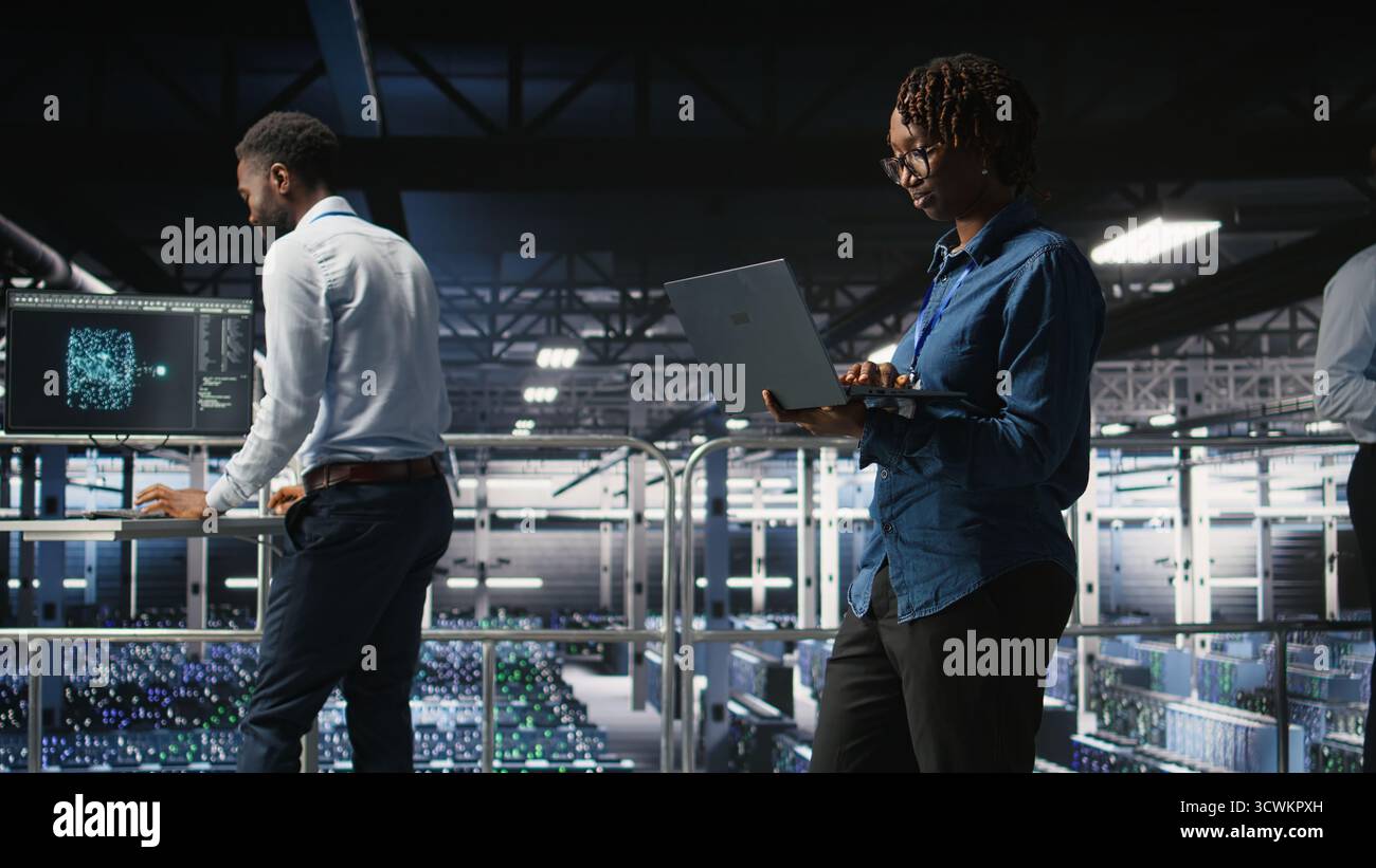 System administrators on data center industrial platform analyzing performance outputs on laptop. Server hub teamworking colleagues finetuning server rig configurations using notebook, Stock Photo