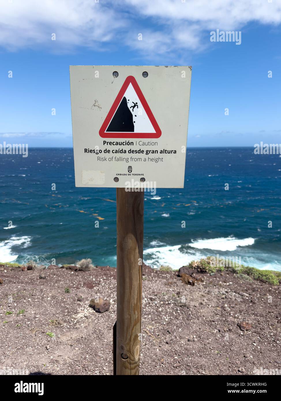 Warning sign cautioning of fall risk by a cliff edge overlooking the ocean with blue sky and white clouds Tenerife Canaries - Smartphone Captured Stock Image
