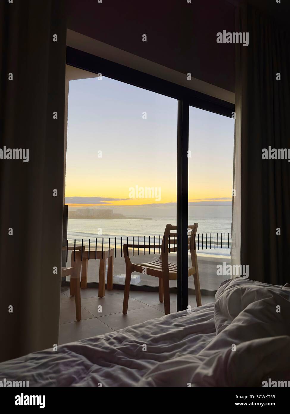 View from a cozy bed looking out to a serene hotel balcony with chairs and table at sunrise over a scenic ocean horizon Tenerife Canaries - Smartphone Captured Stock Image