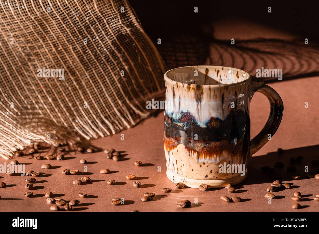 A ceramic coffee mug on a brown background with coffee beans in foreground, morning sunlight Stock Photo