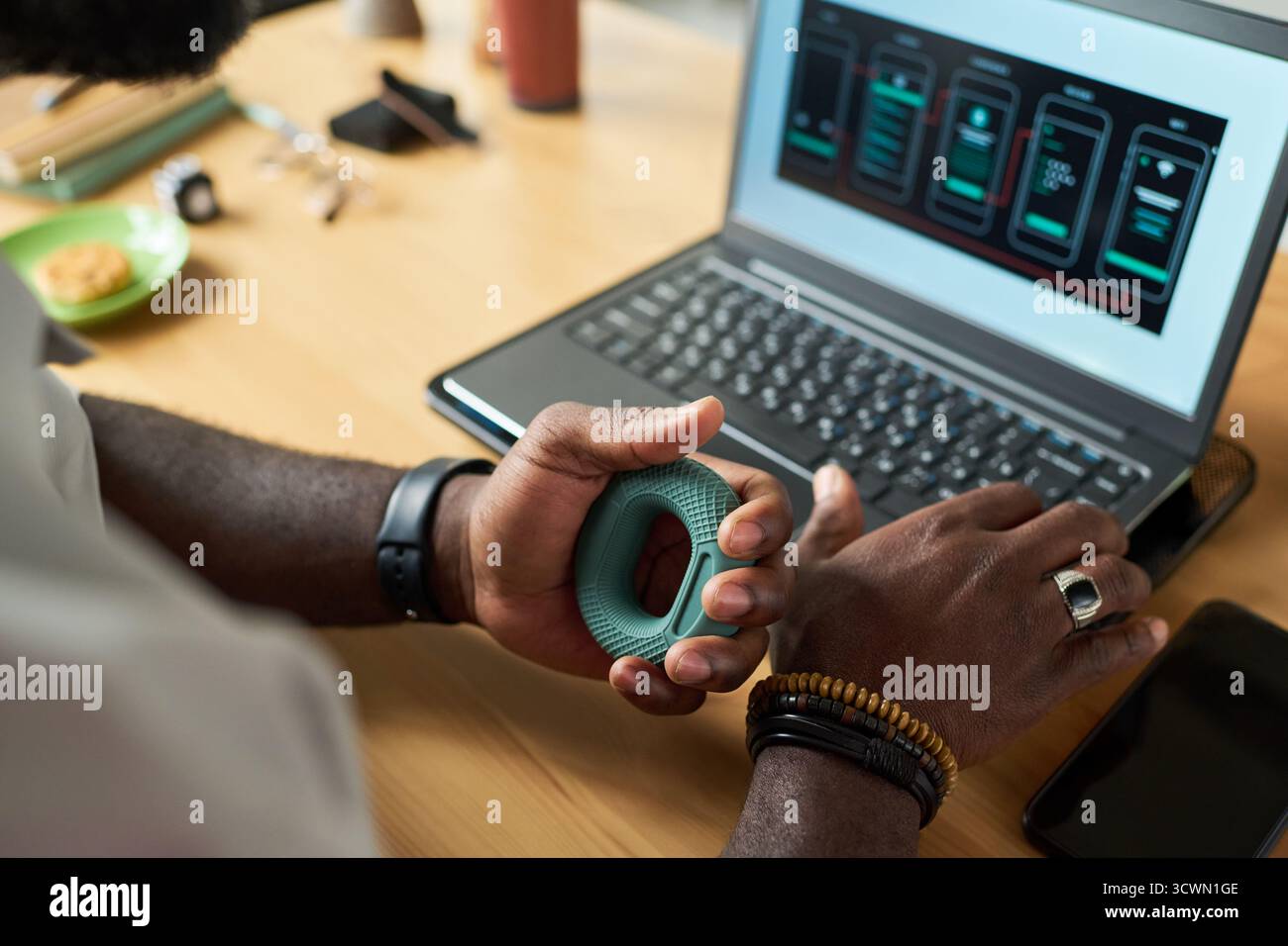Black Man Using Hand Grip Exerciser While Working on Laptop Stock Photo