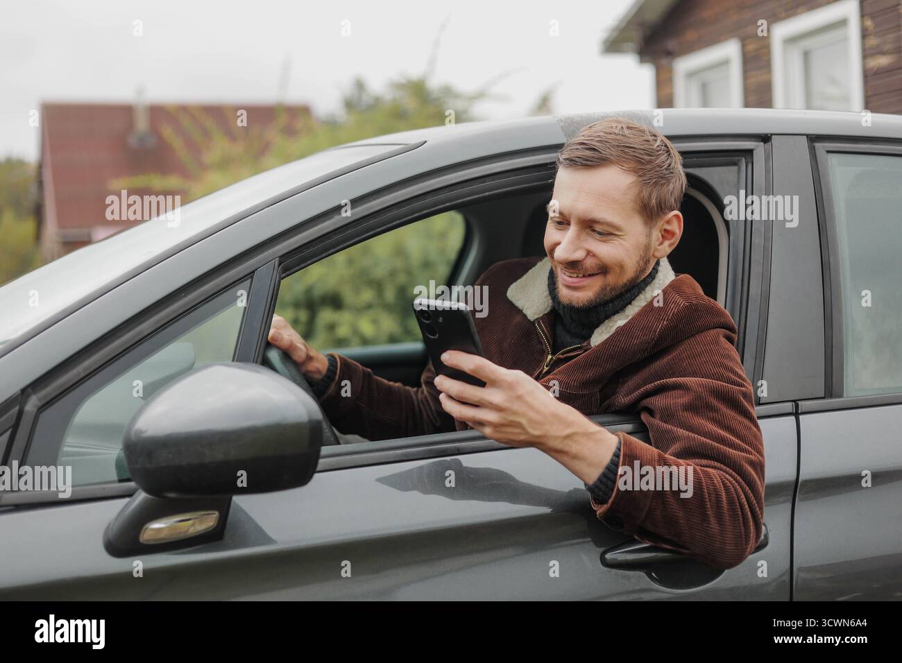Smiling man driver in jacket using smartphone inside the car Stock Photo