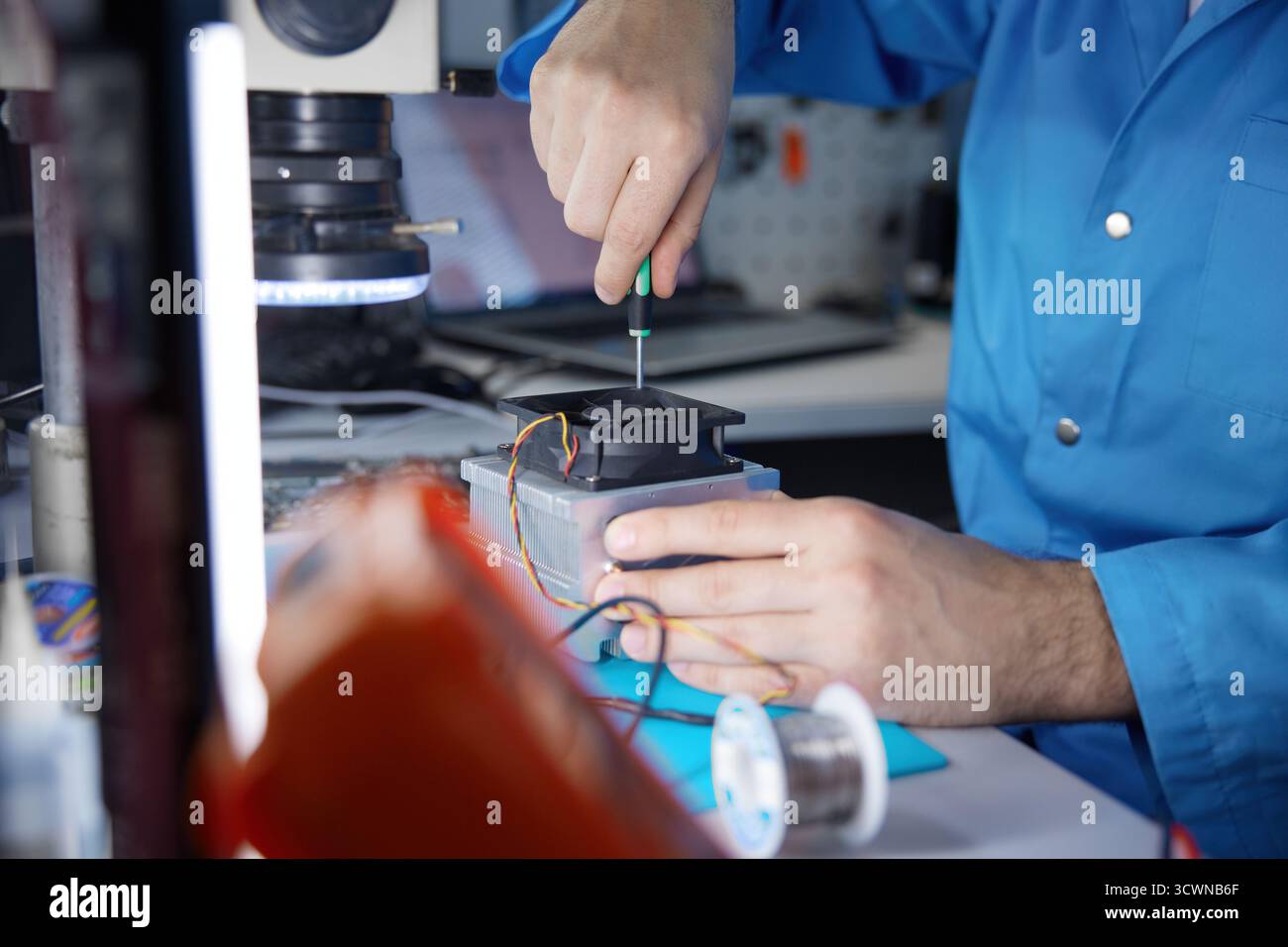 A technician is carefully repairing a circuit board with precision tools in a workshop Stock Photo