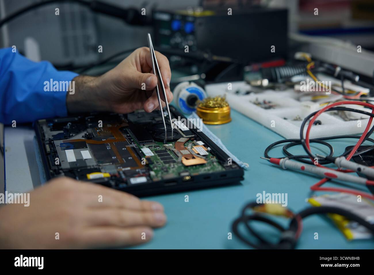 A man works on his laptop while using a soldering iron Stock Photo