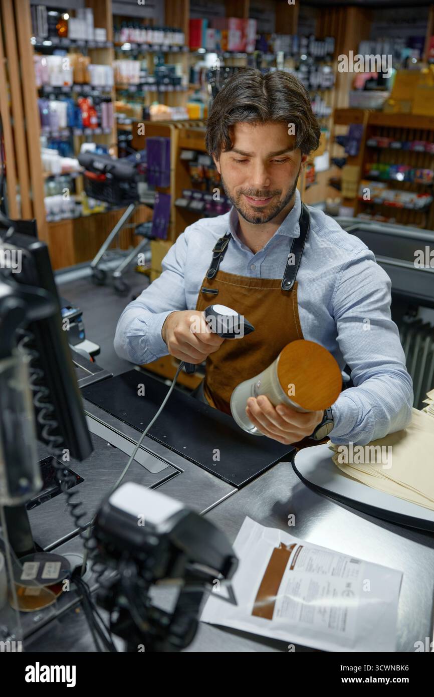 A man cashier wearing an apron is actively using a barcode scanner to scan a candle Stock Photo