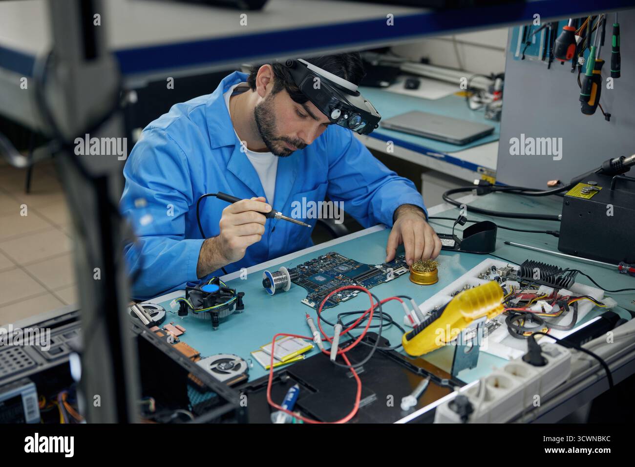 A man soldering technician is fully focused on working on a computer Stock Photo