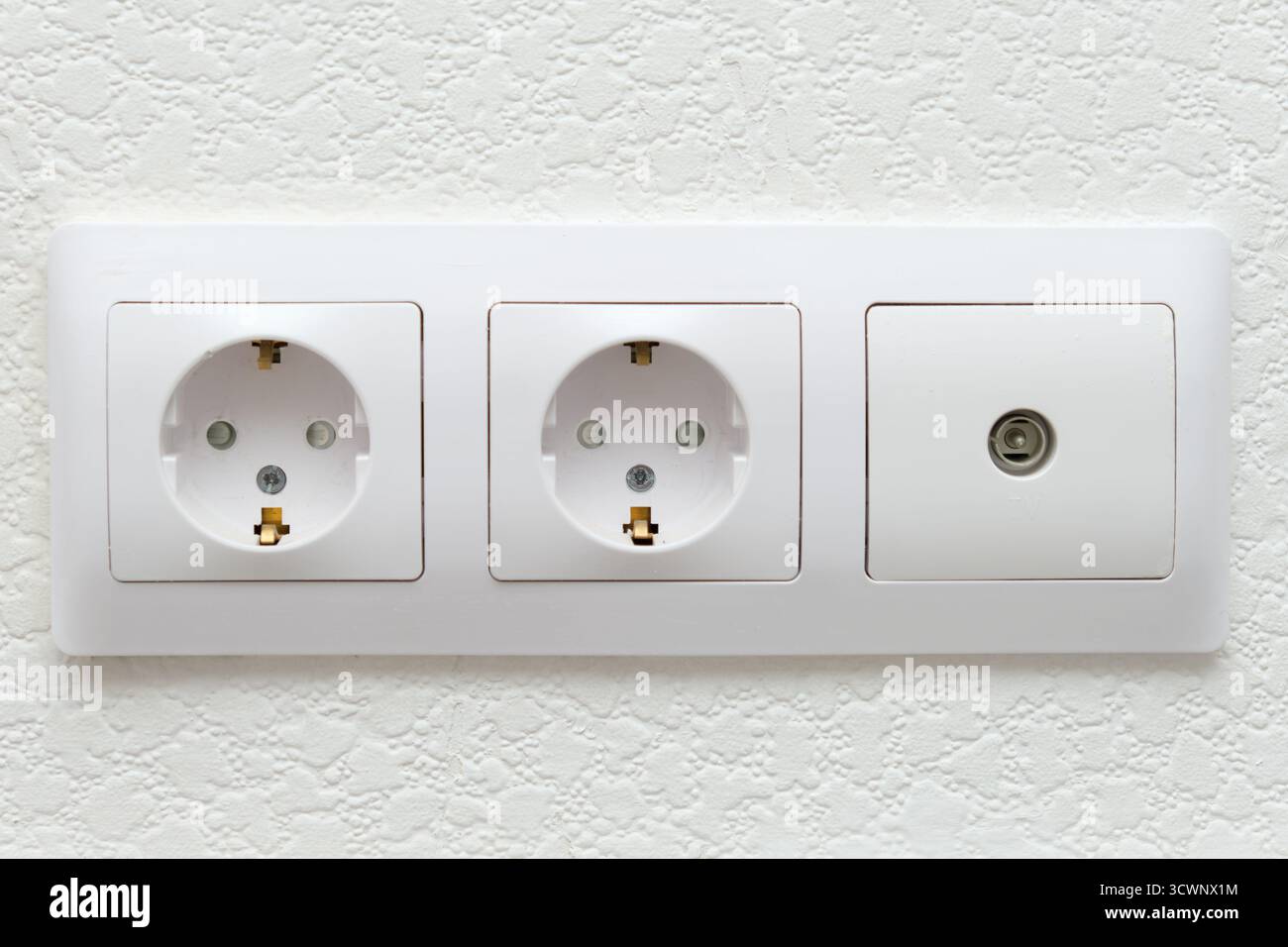 White electrical wall outlet with two power sockets and a TV cable jack. Modern interior electricity connection point for home wiring. Stock Photo