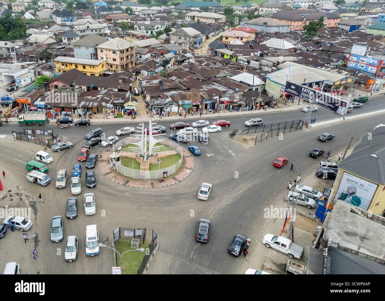 Aerial view of a bustling roundabout with a central monument, cars weaving through traffic, and buildings lining the roadsides, Owerri, Nigeria. Stock Photo