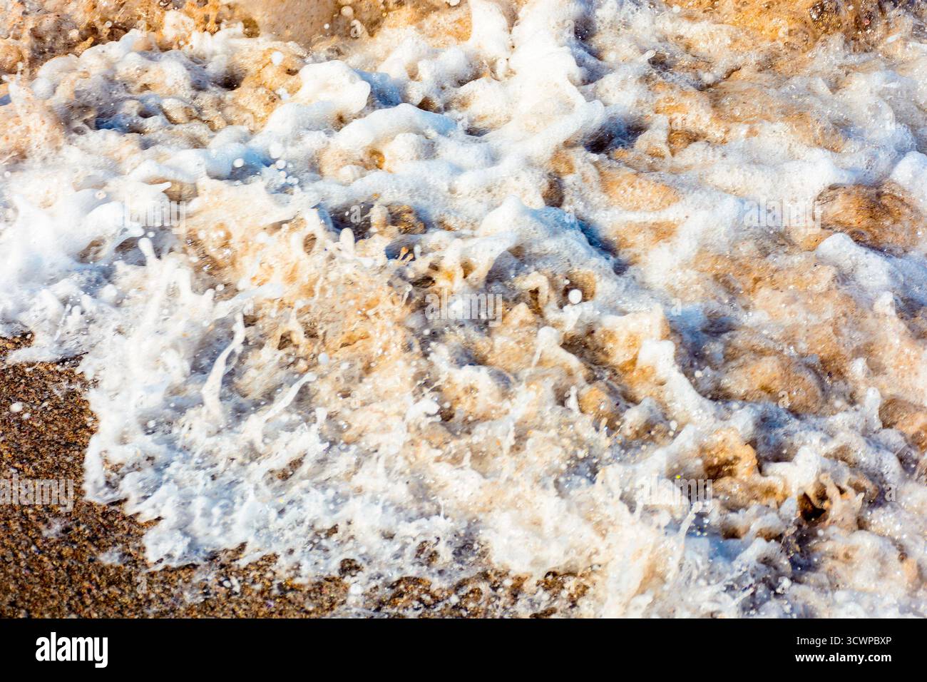 texture of sea foam on the sandy beach. scenic aqua splash. closeup natural abstract background on a sunny day. summer vacation season. frozen moment Stock Photo